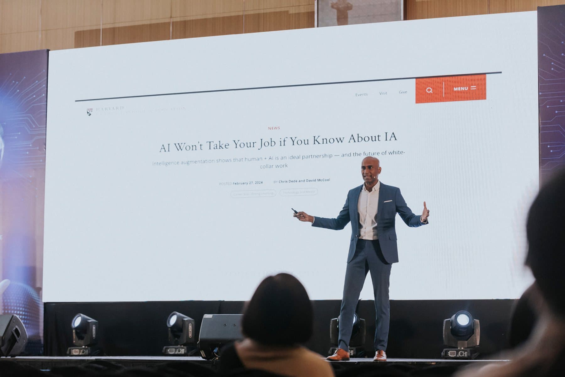 Indhran Seghar on a large stage with a clicker in his hand, in front of a presentation screen, with the audience in the foreground